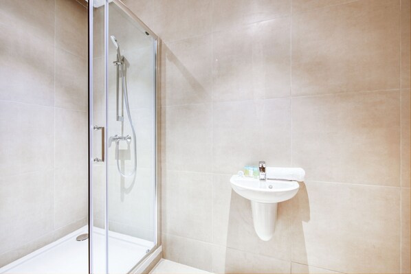 A modern bathroom with a glass-enclosed shower, a white sink, and beige tiles.