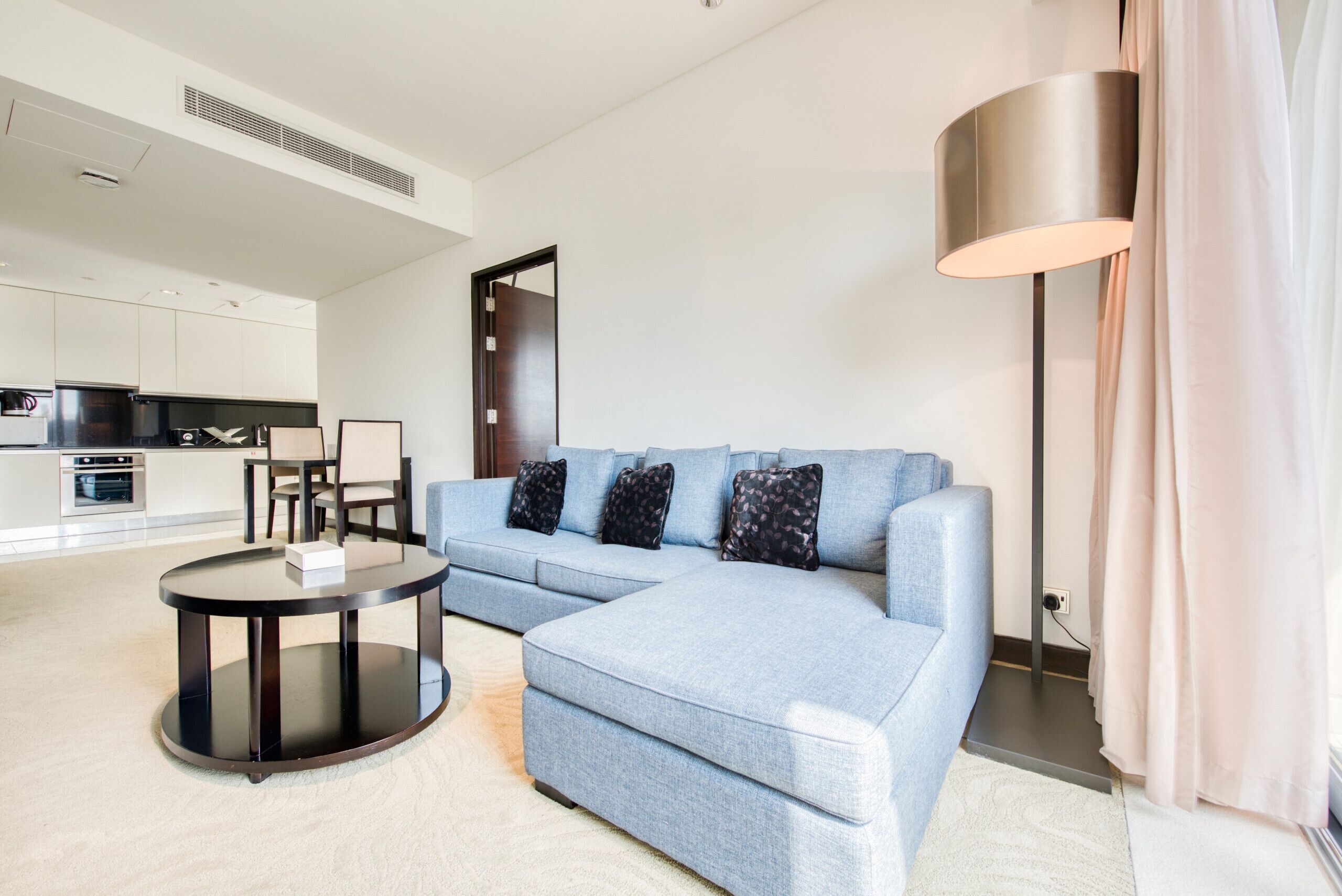 Un salon moderne avec un canapé d’angle, une table basse ronde et un lampadaire.