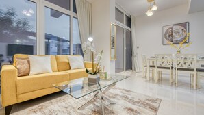 Ein modernes Wohnzimmer mit einem gelben Sofa, einem Glastisch und einem Essbereich mit weißen Stühlen.