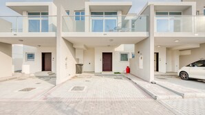 A modern multi-story residential building with balconies, a driveway, and a parked car.