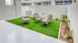 A modern outdoor patio with a green lawn, wicker furniture, and a white tiled floor.