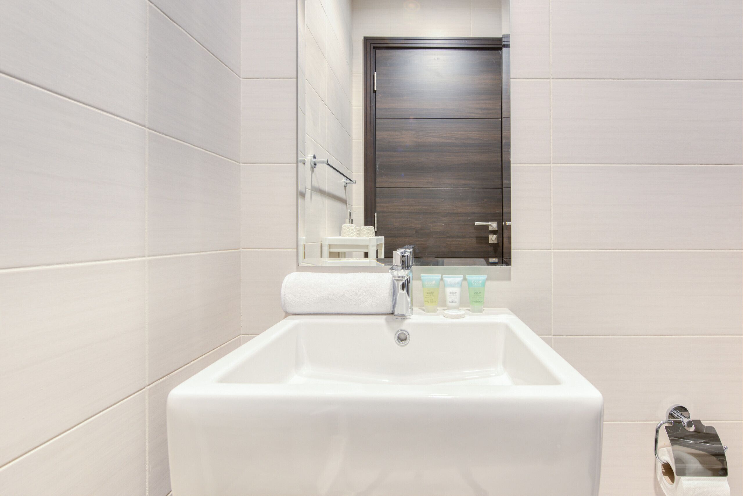 A bathroom with a white sink, a mirror, and a dark wooden door.