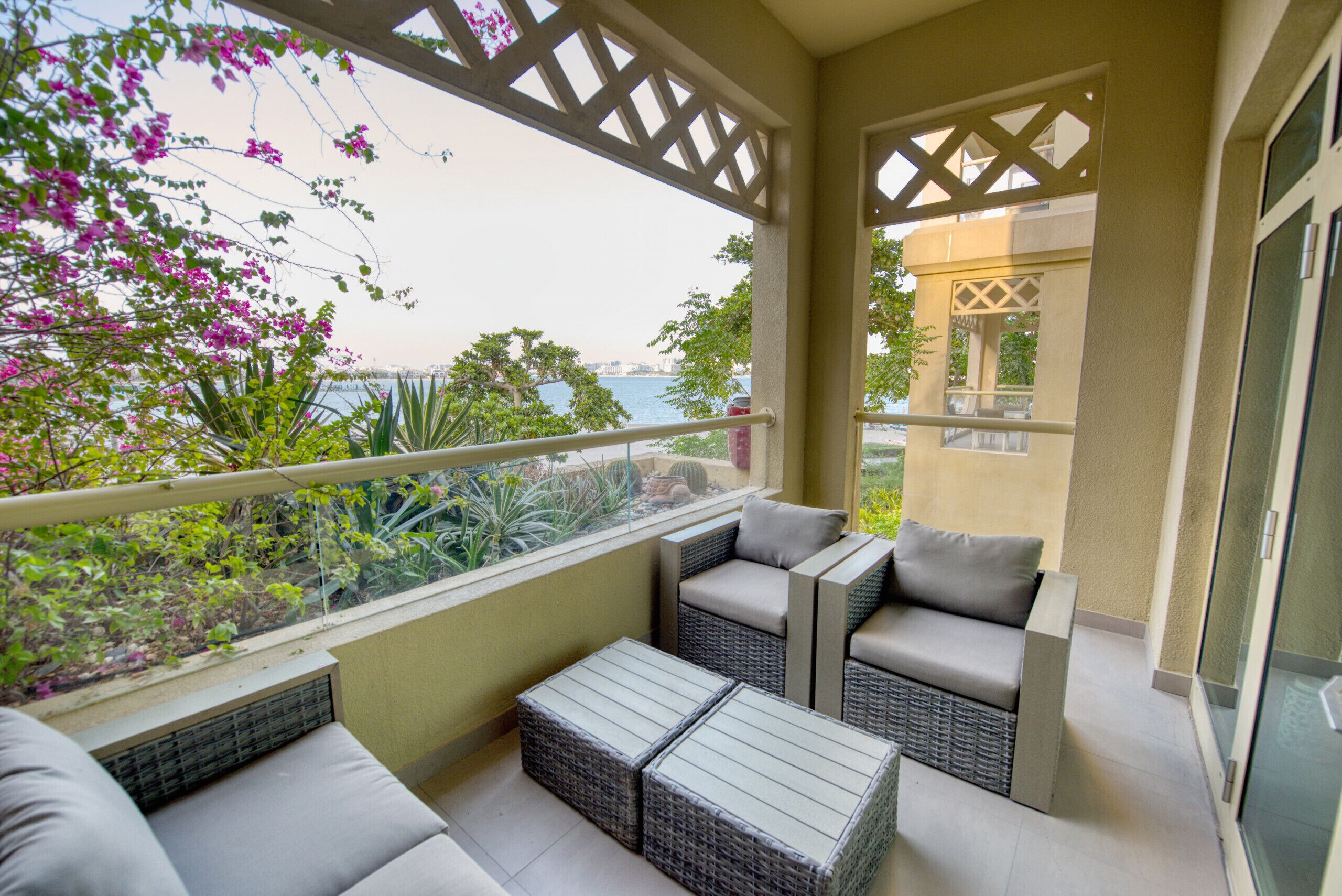 A balcony with wicker furniture, a view of the sea, and lush greenery.