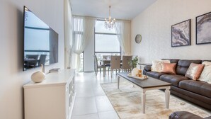 A modern living room with a flat-screen TV, a brown leather sofa, a coffee table, and a dining area with a chandelier. - Fresh 2BR at Mudon Views 4 Dubailand by Deluxe Holiday Homes (Dubai)