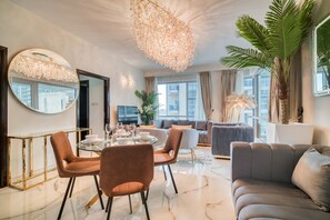 Relax in this stylish living room with a round dining table for four, plush sofa, and armchair, all facing a large window with a city view.