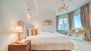 Une chambre spacieuse avec un grand lit, une table de chevet, une lampe, un lustre et une vue sur la ville grâce à de grandes fenêtres.