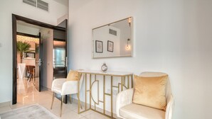 Un salon moderne avec un canapé blanc, une table basse à cadre doré et un fauteuil beige. Un tableau encadré est accroché au mur et une petite horloge est posée sur la table.