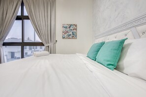 Un lit bien fait, avec du linge de lit blanc et deux coussins turquoise, une œuvre d’art florale accrochée au mur et une fenêtre avec des rideaux.