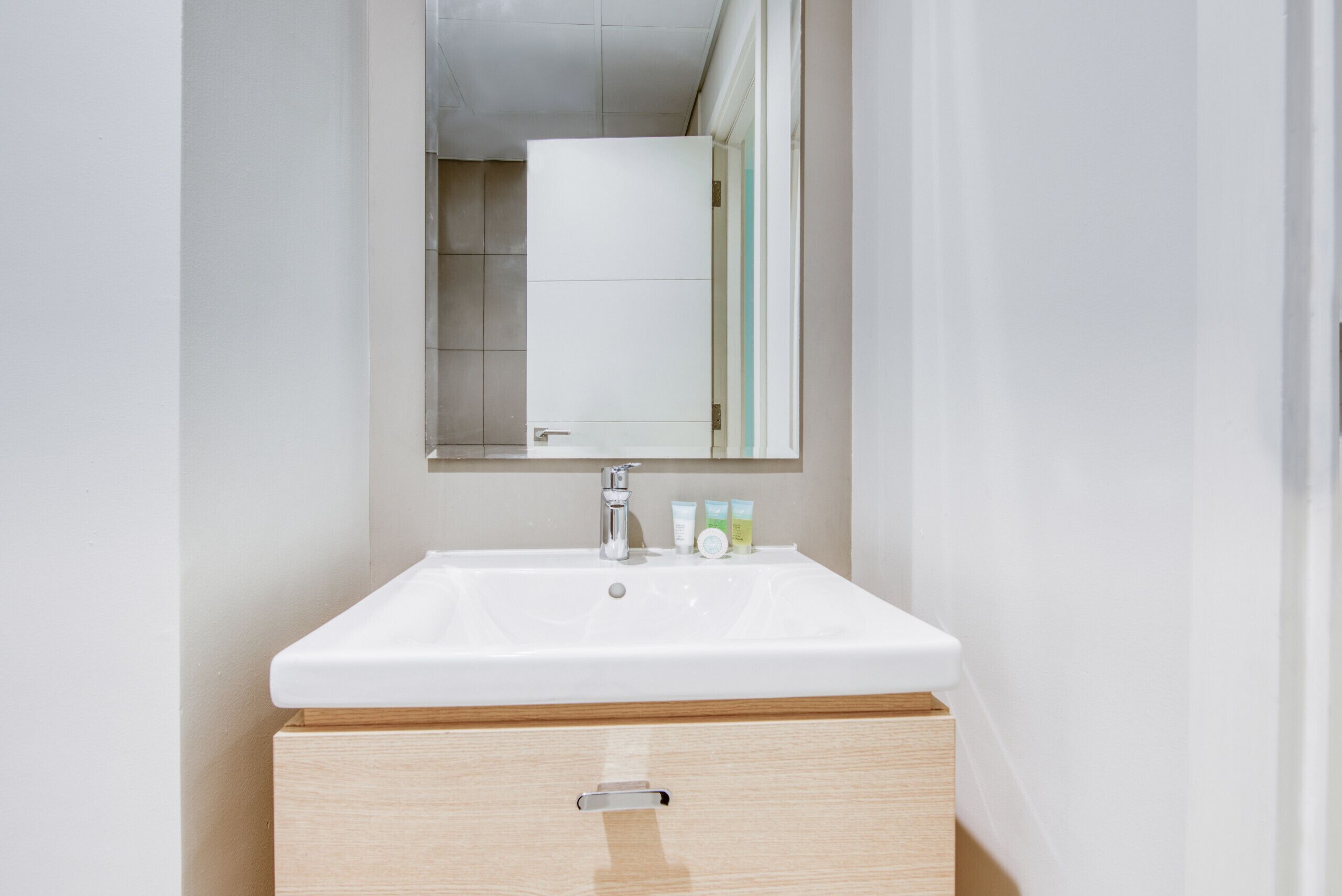 A bathroom with a white sink, a mirror above it, and a wooden cabinet below.