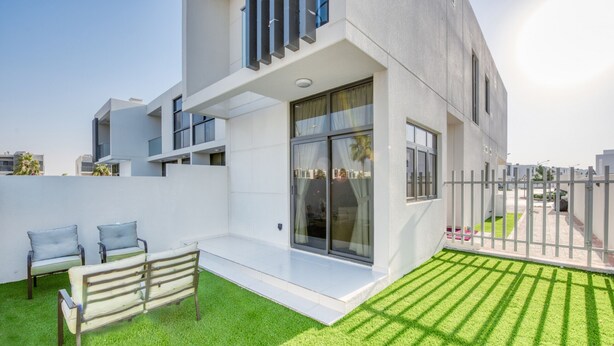 Un bâtiment moderne doté d’un toit plat, de grandes fenêtres et d’un petit espace extérieur aménagé avec deux chaises.