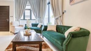 Un salon avec un canapé vert, un fauteuil blanc et une table basse en bois.