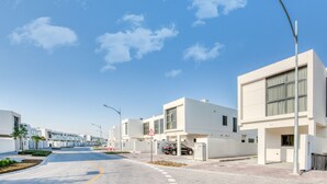 Un quartier résidentiel moderne avec des bâtiments blancs, une route asphaltée et un ciel bleu dégagé.