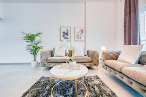 Uma sala de estar moderna com um sofá bege, uma mesa de centro redonda e uma planta em vaso.