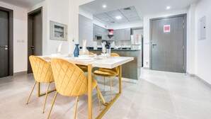 A modern dining area with a white table and gold chairs, a kitchen in the background, and a closed door with a sign. - Whimsical 2BR at Bella Rose Barsha South by Deluxe Holiday Homes (Dubai)