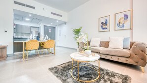 A modern living room with a sofa, a coffee table, and a dining area with chairs and a table. - Whimsical 2BR at Bella Rose Barsha South by Deluxe Holiday Homes (Dubai)