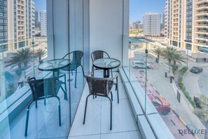 A balcony with two glass tables and four wicker chairs, overlooking a cityscape with tall buildings and a road with cars.