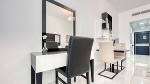 A modern dining area with a white and black table, a black chair, and a beige chair. There is a mirror above the table and a chandelier hanging from the ceiling. - Radiant Studio at Giovanni Boutique Suites DSC by Deluxe Holiday Homes (Dubai)