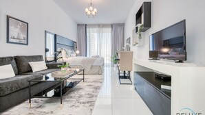 A modern living room with a sofa, coffee table, TV, and a dining area. - Radiant Studio at Giovanni Boutique Suites DSC by Deluxe Holiday Homes (Dubai)