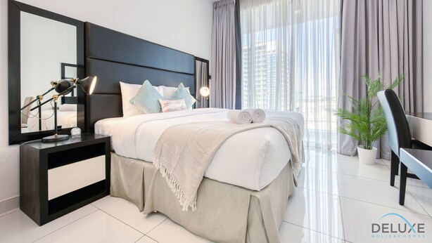 A modern hotel room with a large bed, a bedside table with a lamp, a chair, and a potted plant. - Radiant Studio at Giovanni Boutique Suites DSC by Deluxe Holiday Homes (Dubai)