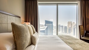 Ein Hotelzimmer mit einem großen Bett, Blick auf die Stadt durch raumhohe Fenster und einem Stadtpanorama im Hintergrund.
