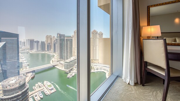 Ein Hotelzimmer in einem Hochhaus mit einem großen Fenster, das einen Blick auf die Stadtlandschaft und einen Fluss bietet.