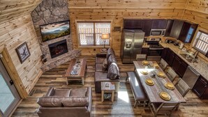 A cozy cabin interior with a stone fireplace, wooden walls, a TV, a dining area with a table set for six, and a kitchen with modern appliances. - New  log cabin ,private indoor heated pool, Pet Friendly, close to town (Pigeon Forge)