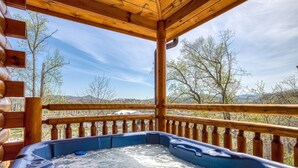 Un bain à remous sur une terrasse en bois, avec vue sur les arbres et les montagnes.