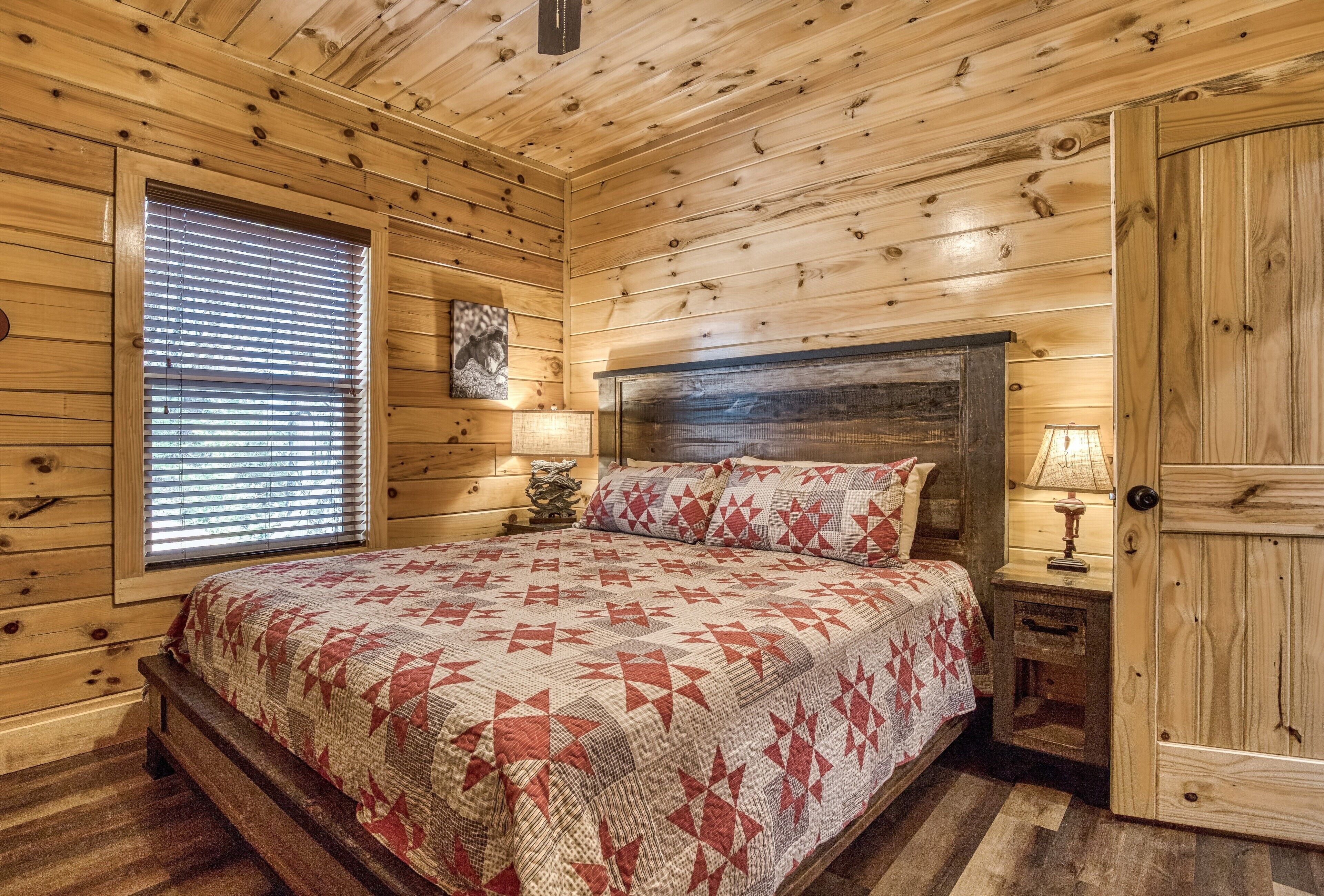 A wooden cabin bedroom with a bed, a nightstand, a lamp, and a door.