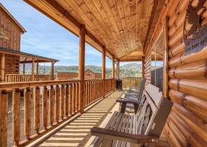 A wooden cabin with a covered porch, outdoor seating, and a view of the surrounding mountains.