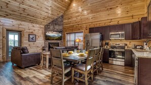 Un intérieur en bois comprenant une table à manger pour quatre personnes, une cuisine équipée d’appareils électroménagers modernes et une cheminée.