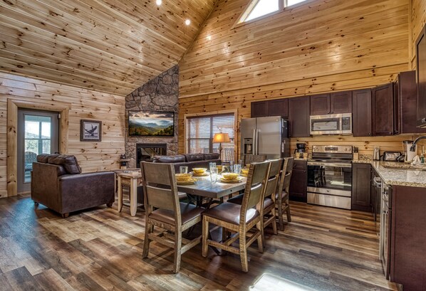 A wooden interior with a dining table set for four, a kitchen with modern appliances, and a fireplace.