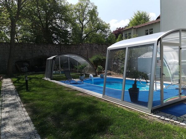 Una piscina techada con cerramiento de vidrio, una silla de descanso y una pared de piedra al fondo.