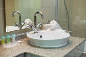 A bathroom with a white sink, two faucets, a mirror, and toiletries on the counter.