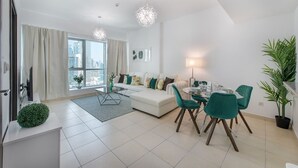 Un salón moderno con un sofá blanco, sillas color turquesa, una mesa de comedor y un amplio ventanal con vistas a la ciudad.