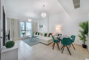 A modern living room with a white sofa, teal chairs, a dining table, and a large window offering a city view.
