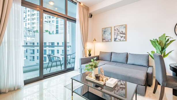 Un salon moderne avec une table basse en verre, un canapé gris et de grandes fenêtres avec des rideaux.