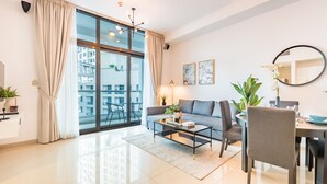 Un salon moderne avec un canapé, une table basse et une table à manger. On y trouve une grande fenêtre avec des rideaux, un miroir rond et une plante en pot.