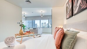 Una habitación de hotel moderna con una cama grande, vistas a la ciudad, una zona de comedor con mesa y sillas, y un ventanal amplio.
