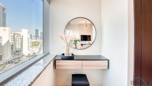 Un baño moderno con un ventanal grande, un espejo redondo, un tocador negro y vistas de la ciudad.