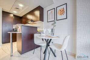 Cocina moderna con armarios de madera oscura, encimera blanca y zona de comedor con dos sillas blancas y una mesa pequeña.