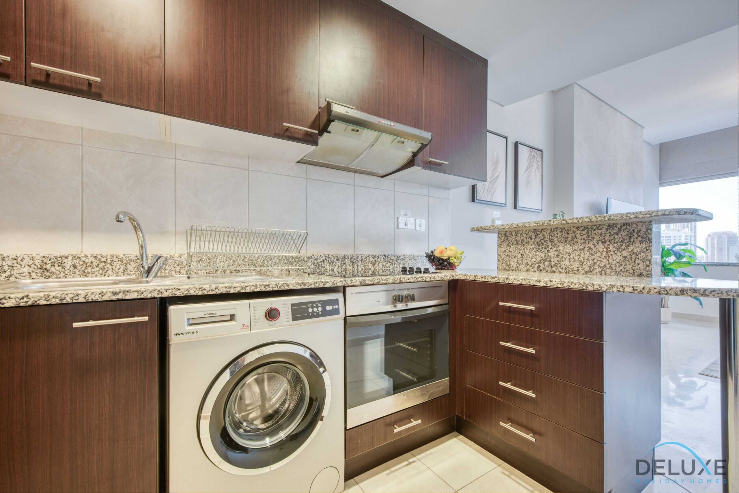 Una cocina moderna con lavadora y secadora integradas, armarios de madera y encimeras de granito.