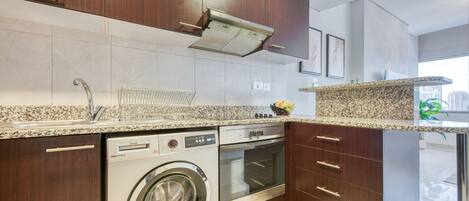 A modern kitchen with a built-in washer and dryer, wooden cabinets, and granite countertops.
