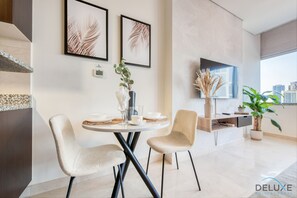 A modern living room with a round dining table, two chairs, a flat-screen TV, and a large window with a city view.