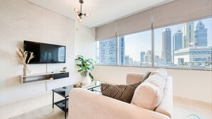 A modern living room with a large TV, a sofa, a coffee table, and a city view through large windows. - Calm Studio at Sky Gardens DIFC by Deluxe Holiday Homes (Dubai)