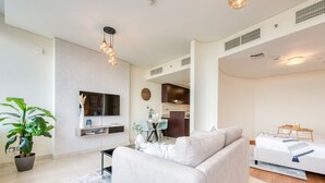 A modern living room with a sofa, TV, dining area, and kitchenette.