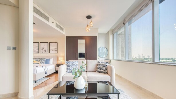 A modern living room with a sofa, coffee table, and a large window offering a city view.