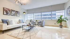 A spacious living room with a white sofa, two armchairs, a coffee table, and a large window with blinds. - Gorgeous 1BR at Sky Gardens DIFC by Deluxe Holiday Homes (Dubai)
