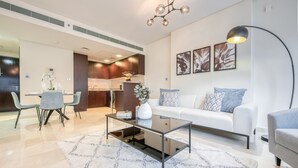 A modern living room with a glass coffee table, a white sofa, and a dining area with a table set for two. - Gorgeous 1BR at Sky Gardens DIFC by Deluxe Holiday Homes (Dubai)