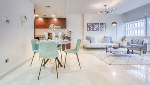 A modern living room with a sofa, coffee table, and dining area with chairs. - Gorgeous 1BR at Sky Gardens DIFC by Deluxe Holiday Homes (Dubai)