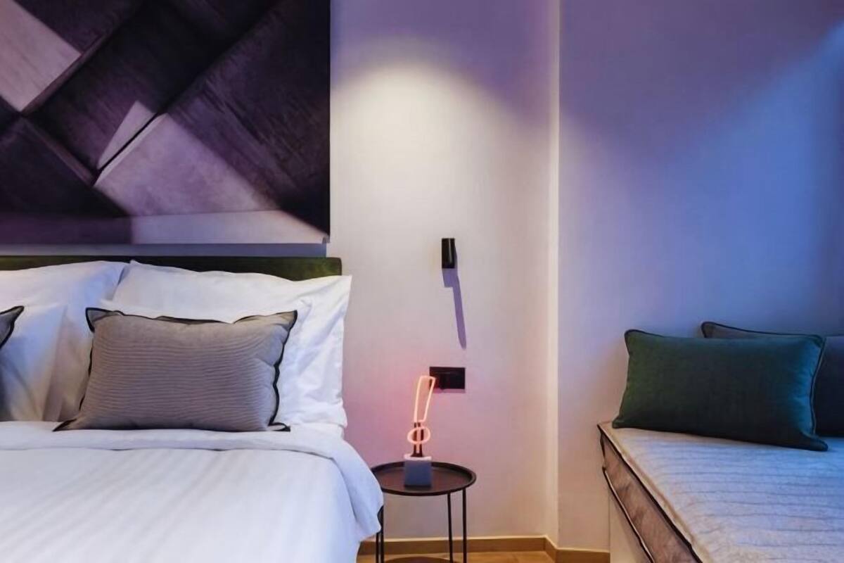 A hotel room with a bed, bedside table, and a wall-mounted light fixture.